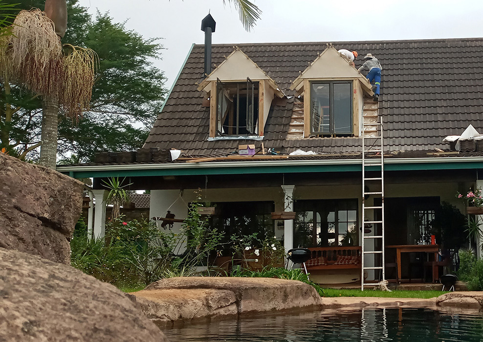 This is a photo of a roof room conversion at a property in Winston Park, KZN. 
                            The photo shows work being done to build two large dorma windows with the same roof tiles and fascia board style as the rest of the house.