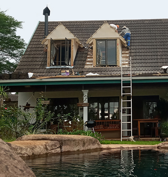 This is a photo of a roof room conversion at a property in Winston Park, KZN. 
                            The photo shows work being done to build two large dorma windows with the same roof tiles and fascia board style as the rest of the house.